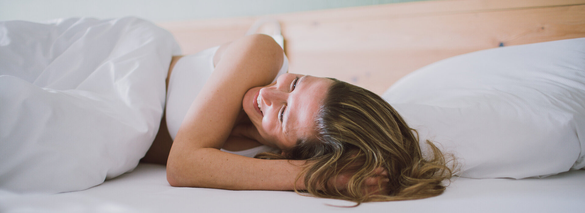 Eine Frau wacht ausgeschlafen und gut gelaunt auf, sie lächelt dabei.