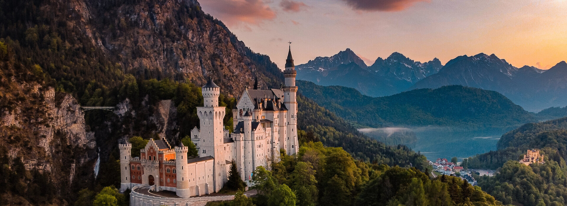 Das Bild fängt das majestätische Schloss Neuschwanstein im Sonnenuntergang ein, im Hintergrund Schloss Hohenschwangau und der Alpsee