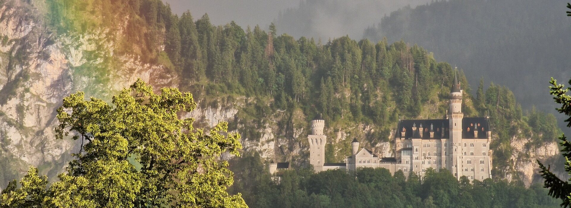 Das Foto zeigt Schloss Neuschwanstein bei Füssen im Allgäu mit einem Regenbogen.