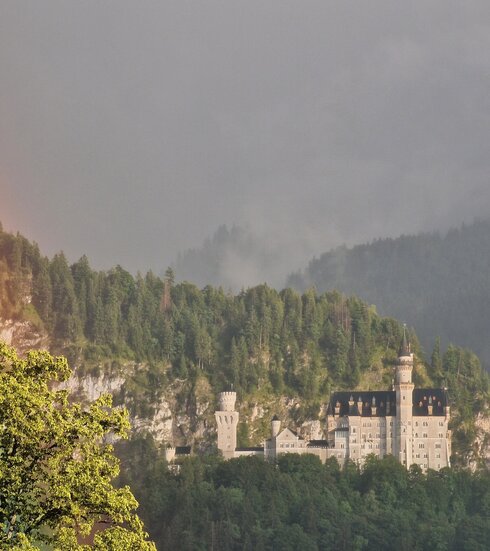 Das Foto zeigt Schloss Neuschwanstein bei Füssen im Allgäu mit einem Regenbogen.