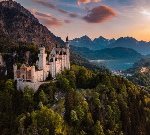 Das Bild fängt das majestätische Schloss Neuschwanstein im Sonnenuntergang ein, im Hintergrund Schloss Hohenschwangau und der Alpsee