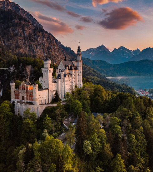 Das Bild fängt das majestätische Schloss Neuschwanstein im Sonnenuntergang ein, im Hintergrund Schloss Hohenschwangau und der Alpsee