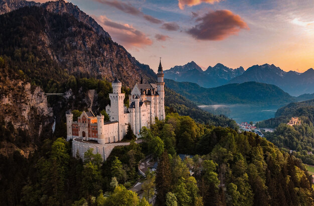 Das Bild fängt das majestätische Schloss Neuschwanstein im Sonnenuntergang ein, im Hintergrund Schloss Hohenschwangau und der Alpsee