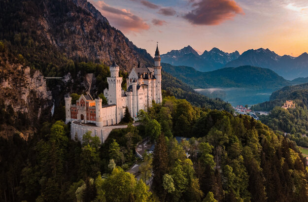 Das Bild fängt das majestätische Schloss Neuschwanstein im Sonnenuntergang ein, im Hintergrund Schloss Hohenschwangau und der Alpsee