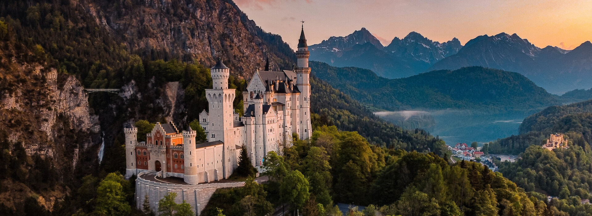 Das Bild fängt das majestätische Schloss Neuschwanstein im Sonnenuntergang ein, im Hintergrund Schloss Hohenschwangau und der Alpsee
