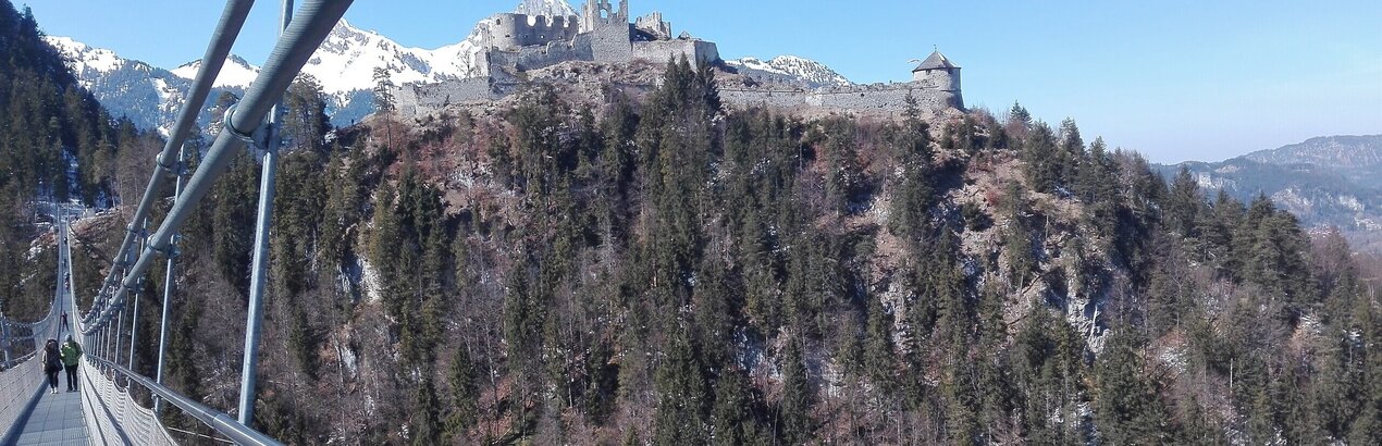  Das Bild zeigt einen atemberaubenden Ausblick auf eine Burg, die auf einem Felsen thront. Die aus Stein errichtete Burg steht majestätisch vor dem Hintergrund eines klaren blauen Himmels. Der Felsen, der mit üppigem Grün bedeckt ist, fügt der Szene die Schönheit der Natur hinzu. Eine Brücke aus Metall spannt sich über das Bild und bietet dem Betrachter eine Aussichtspunkt. Die Brücke, mit ihrer soliden Struktur, scheint ein beliebter Ort für Touristen zu sein, wie die Menschen, die zu sehen sind, die über sie gehen. Die gesamte Szene ist ein harmonisches Zusammenspiel von Architektur und Natur und bietet eine einzigartige Perspektive auf die Burg und ihre Umgebung.