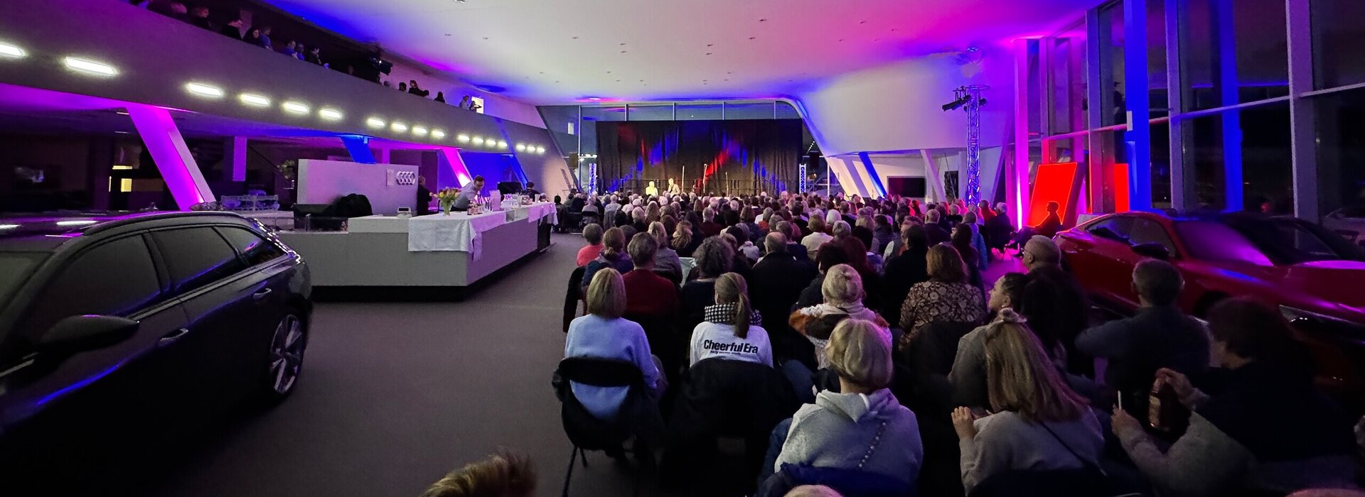 Das Bild zeigt mehrere Personen in Neoprenanzügen im knietiefen Wasser stehen. Alle tragen unterschiedliche Mützen und halten brennende Fackeln in den Händen. Es Dämmert. Es ist schon fast dunkel.  Auf der linken Seite des Bildes steht ein Auto. Auf einem Tresen sind Getränke und Gläser zu sehen. Im Hintergrund sieht man eine Bühne mit mehreren Musikern darauf. 