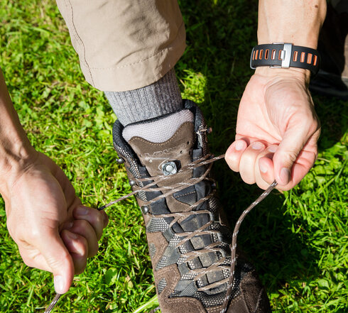 Das Bild zeigt das Detail eines braunen Wanderschuhs von oben. Eine Person bindet gerade die Schuhbändel. 