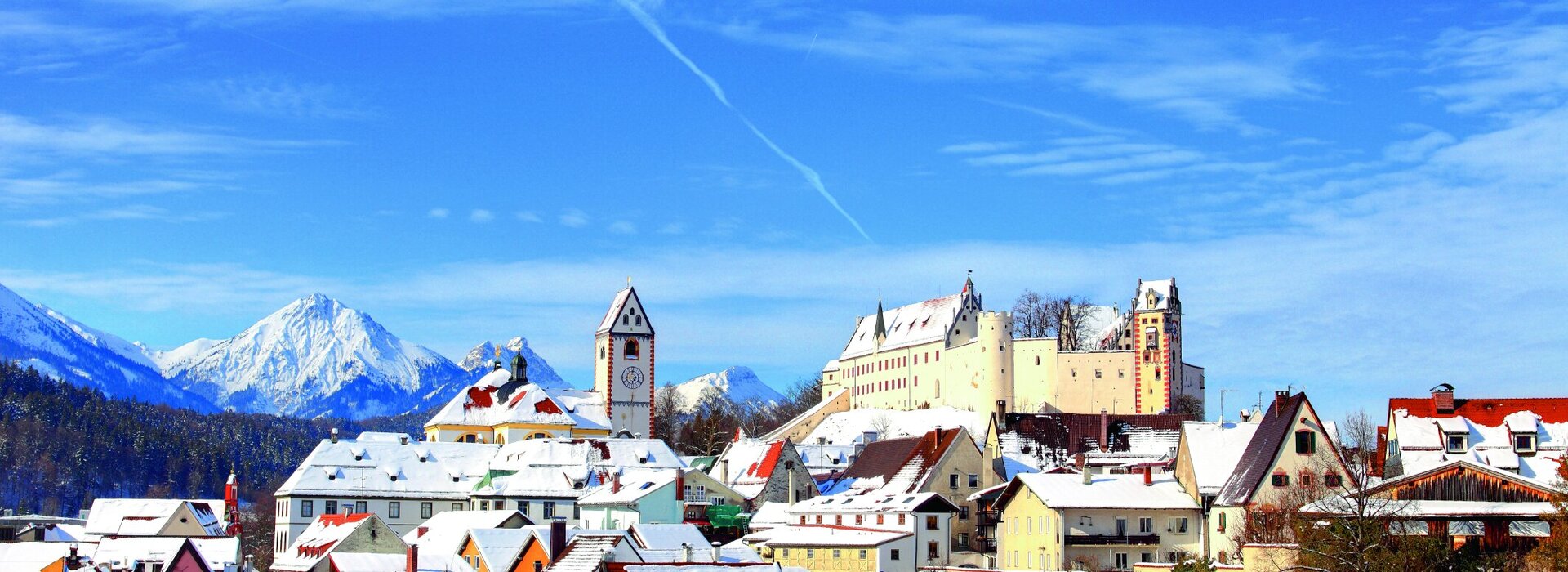 Das Bild fängt den atemberaubenden Anblick der mittelalterlichen Stadt Füssen in Deutschland ein. Die Stadt befindet sich vor majestätischen Bergen umgeben. Die Architektur der Stadt wird durch bunte Gebäude gekennzeichnet, jedes mit einem einzigartigen Charme. Die Gebäude sind mit Schnee verziert, was dem Szenario einen Hauch von Winter verleiht. Die Stadt ist von einer verriegelten Mauer umgeben, ein Zeugnis für ihre historische Bedeutung. Der Himmel darüber ist in einem klaren Blau, der eine herrliche Kulisse zur Stadt bildet. Das Bild ist eine atemberaubende Darstellung der reichen Geschichte und malerischen Schönheit der Stadt.