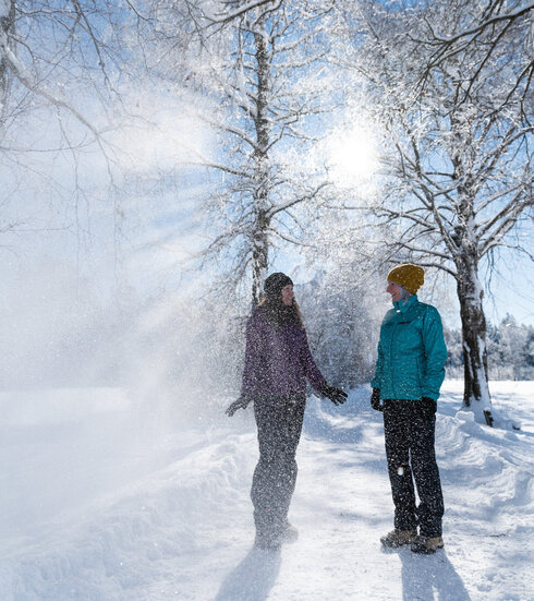 Ein Pärchen lacht im winterlichen Sonnenschein unter mit Schnee bepuderten Bäumen in Füssen