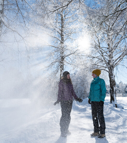 Ein Pärchen lacht im winterlichen Sonnenschein unter mit Schnee bepuderten Bäumen in Füssen