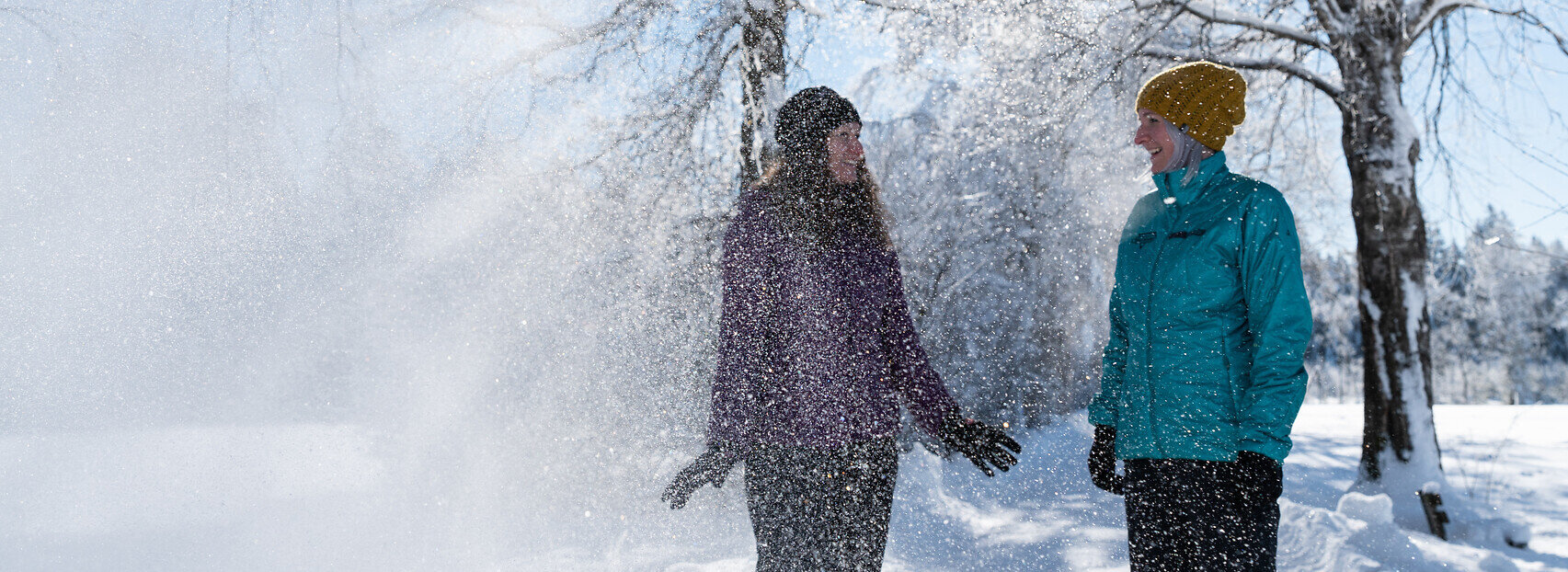 Ein Pärchen lacht im winterlichen Sonnenschein unter mit Schnee bepuderten Bäumen in Füssen