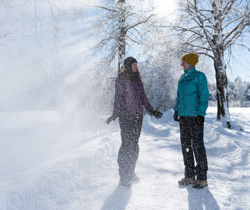 Ein Pärchen lacht im winterlichen Sonnenschein unter mit Schnee bepuderten Bäumen in Füssen