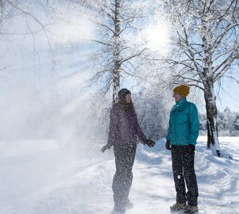 Ein Pärchen lacht im winterlichen Sonnenschein unter mit Schnee bepuderten Bäumen in Füssen