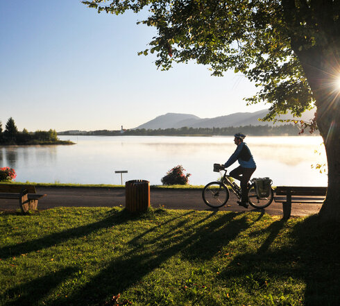 Ein Fahrradfahrer fährt am Ufer Hopfensees ein Tourenrad im Sonnenuntergang