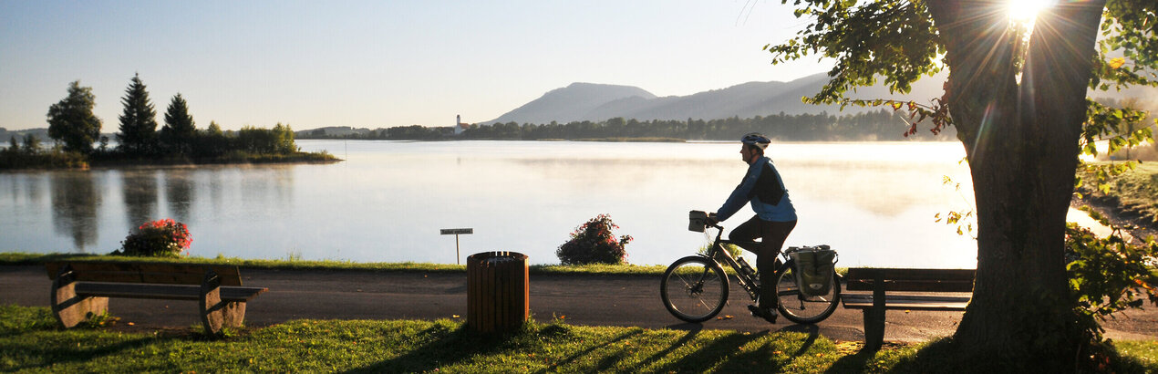 Ein Fahrradfahrer fährt am Ufer Hopfensees ein Tourenrad im Sonnenuntergang