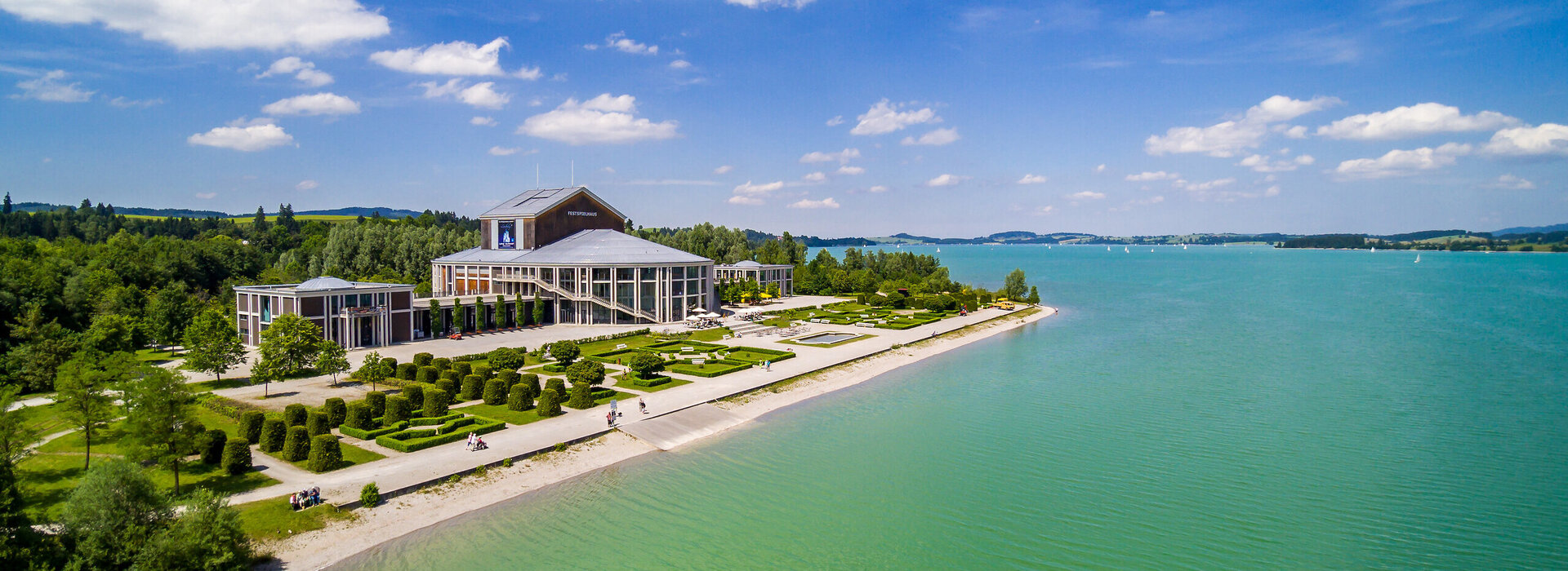 Panoramafoto: Das Festpielhaus Neuschwanstein am Ufer des smaragdgrünen Forggensees im Sommer