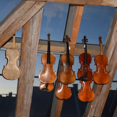 Das Foto zeigt eine Reihe reparaturbedürftiger Geigen vor dem Dachfenster in der Geigenbauerwerkstatt von Pierre und Eric Chaubert in Füssen im Allgäu.