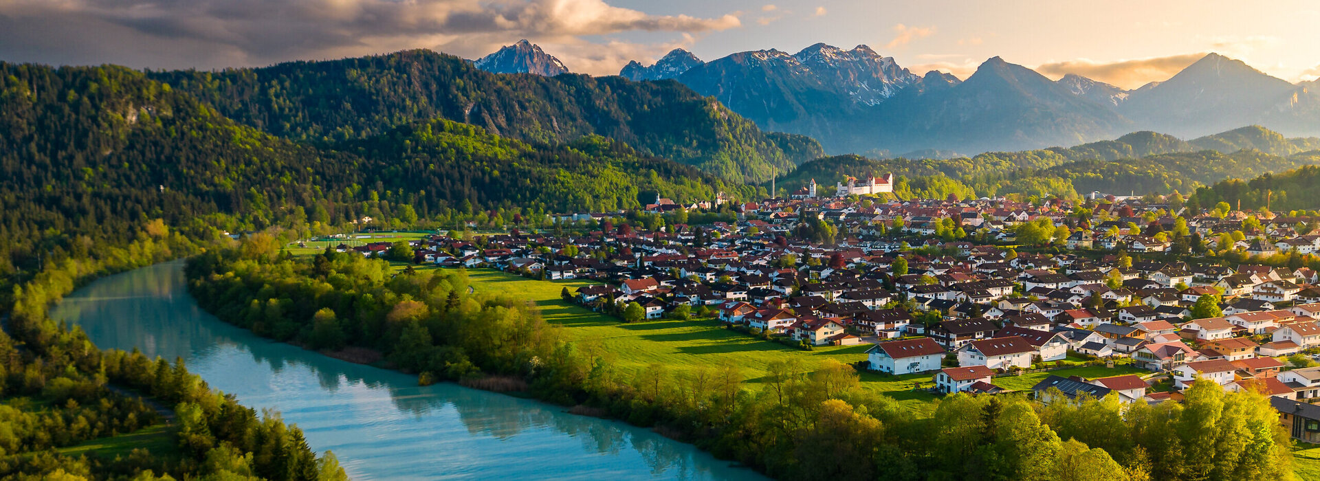 Das Foto wurde mit einer Kameradrohne gemacht und zeigt Füssen im Allgäu und den Lech von oben. Im Hintergrund sieht man die Alpengipfel unr um Füssen.