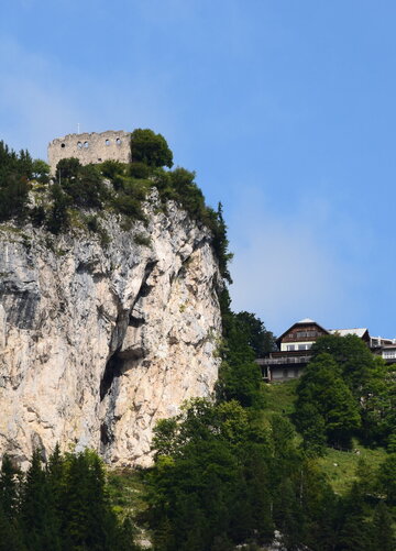 Das Bild zeigt einen atemberaubenden Ausblick auf eine Burg-ähnliche Struktur, die sich auf einem steilen Felsvorsprung befindet. Die Burg in Stein erbaut, steht majestätisch vor einem klaren blauen Himmel. Der Felsvorsprung selbst ist ein Spektakel, mit üppigem grünen Laubwerk und Büschen, die eine Naturpracht hinzufügen. Die Lage der Burg auf dem Felsvorsprung bietet einen Vorteilspunkt mit einer Panoramasicht auf das umliegende Landesinnere. Das Bild ist ein Zeugnis der architektonischen Geschicklichkeit der Vergangenheit und steht kraftvoll unter den natürlichen Elementen.
