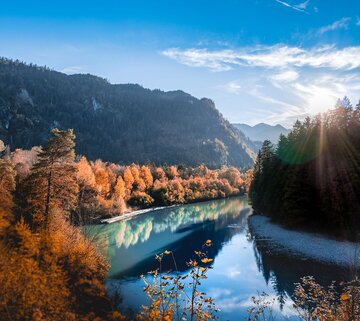 Das Bild zeigt einen Fluss umgeben von Wald mit herbstlich rot gefärbtem Laub.