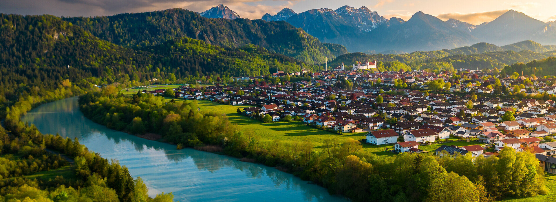 Das Foto wurde mit einer Kameradrohne gemacht und zeigt Füssen im Allgäu und den Lech von oben. Im Hintergrund sieht man die Alpengipfel unr um Füssen.