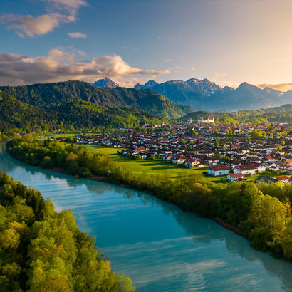 Das Foto wurde mit einer Kameradrohne gemacht und zeigt Füssen im Allgäu und den Lech von oben. Im Hintergrund sieht man die Alpengipfel unr um Füssen.