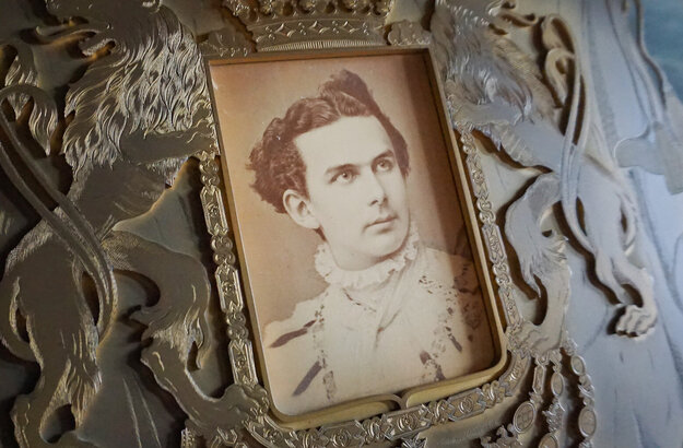 Das Bild zeigt ein Schwarz/weiß Foto von König Ludwig, welches liebevoll in eine verziehrte und geschnitze Holztafel eingebetet wurde. 