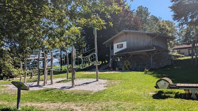 Das Bild zeigt ein paar Spielgeräte eines Spielplatzes in einer grünen Wiese.