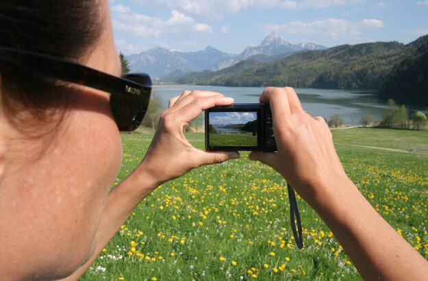 Das Foto zeigt eine Frau, die auf einer Wiese am Weißensee bei Füssen im Allgäu das Alpenpanorama fotografiert.