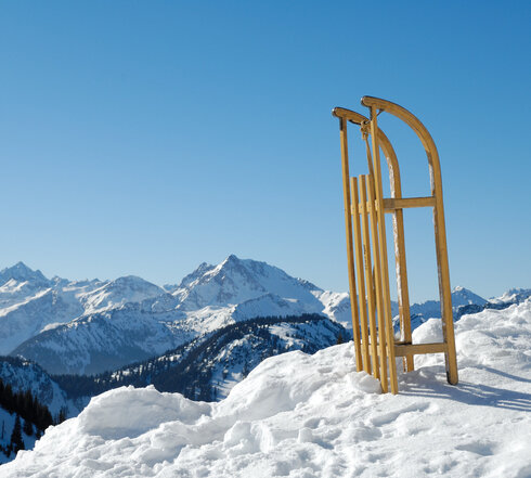 Das Bild zeigt eine atemberaubende Landschaft eines schneebedeckten Gebirges. Im Mittelpunkt steht eine hölzerne Struktur, die sich stolz vor dem Panorama der Berge erhebt. Die Struktur mit ihren vier hölzernen Pfosten ist auf der linken Seite des Bildes positioniert. Die Pfosten sind in einer quadratischen Formation angeordnet, was ein Gefühl von Ausgeglichenheit und Harmonie erzeugt. Der hölzerne Charakter der Struktur kontrastiert wunderschön mit dem reinen weißen Schnee, der die Berge bedeckt. Die Berge selbst sind majestätisch, ihre Gipfel reichen hoch in den klaren blauen Himmel hinauf. Das Bild wurde von einer niedrigen Perspektive aus aufgenommen, was die Großartigkeit der Berge und der Struktur hervorhebt. Die Gesamtansicht des Bildes erzeugt ein Gefühl der Ruhe und einer eindrucksvollen Schönheit.
