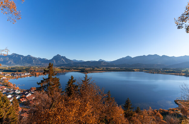 Das Herbstfoto zeigt die Aussicht auf den Hopfensee und die Alpengipfel rund um Füssen im Allgäu von der Burgruine Hopfen aus.
