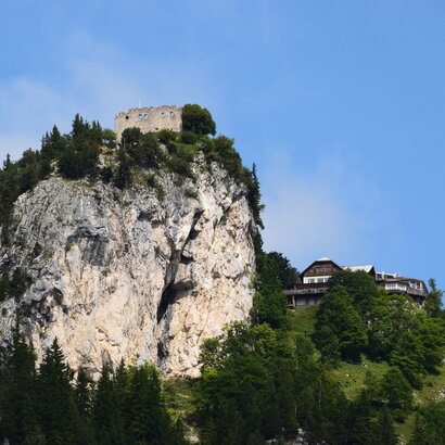 Das Bild zeigt einen atemberaubenden Ausblick auf eine Burg-ähnliche Struktur, die sich auf einem steilen Felsvorsprung befindet. Die Burg in Stein erbaut, steht majestätisch vor einem klaren blauen Himmel. Der Felsvorsprung selbst ist ein Spektakel, mit üppigem grünen Laubwerk und Büschen, die eine Naturpracht hinzufügen. Die Lage der Burg auf dem Felsvorsprung bietet einen Vorteilspunkt mit einer Panoramasicht auf das umliegende Landesinnere. Das Bild ist ein Zeugnis der architektonischen Geschicklichkeit der Vergangenheit und steht kraftvoll unter den natürlichen Elementen.