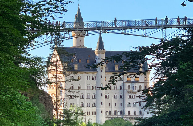 Das Foto zeigt im Vordergrund die Marienbrücke mit einigen Besuchern, dahinter Schloss Neuschwanstein bei Füssen im Allgäu.