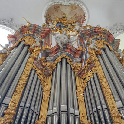 Das Bild zeigt die Pfeifen einer Kirchenorgel, die mit buntem Stuck ringsum reich verziert sind. Das Foto ist von unten aufgenommen.  