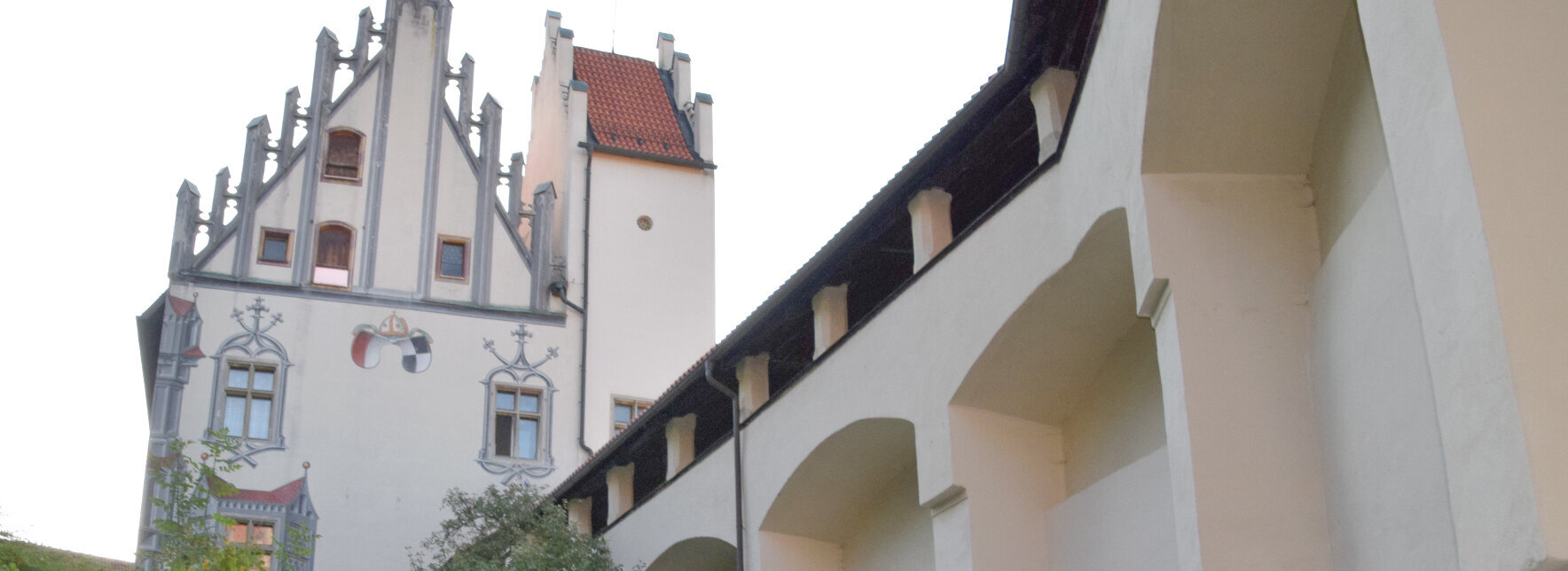 Das Bild zeigt eine Gruppe Menschen, die dem Betrachter weggewandt sind. Die Gruppe steht im Schlosshof des Hohen Schlosses und laufen in Richtung des Hauptgebäudes. Die Abendsonne taucht die Szene in ein warmes Licht. 